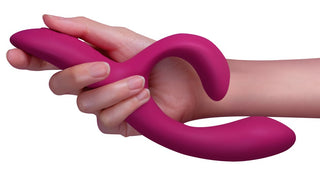 En hand håller We-Vibe Nova 2 Rabbitvibrator, en rosa, böjd, flexibel vibrator med två rundade ändar, mot en vit bakgrund.