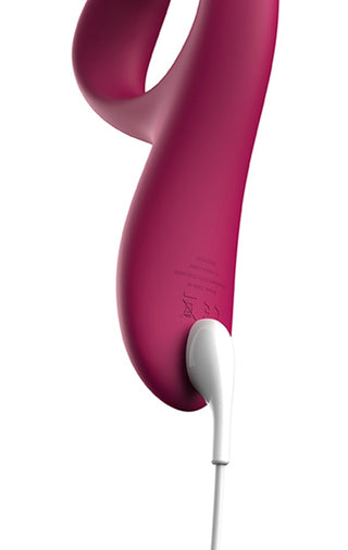 En rosa, böjd We-Vibe Nova 2 Rabbitvibrator laddas med en vit kabel mot en vit bakgrund.