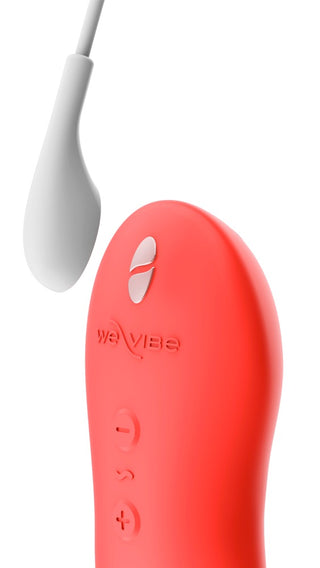 En röd We-Vibe Touch X med vita kontrollknappar och en vit laddningskabel, visas mot en vit bakgrund. Dess vattentäta design garanterar säker och trevlig användning.