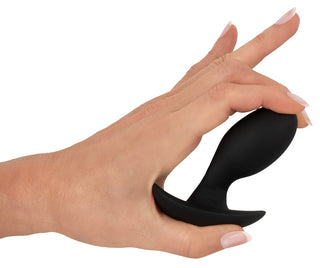 En hand håller den eleganta svarta Anos Vibrerande Buttplug, med en silikondesign med en utsvängd bas, perfekt för utforskning, mot en orörd vit bakgrund.