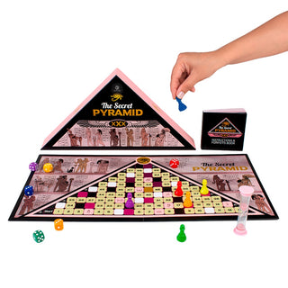 En hand flyttar en spelpjäs på Erotiskt Spel Pyramid, ett vuxenspel med egyptiskt tema, med tärningar, timer och kort synliga.