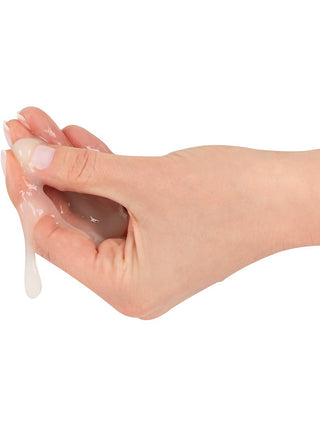 En hand som pressar en klar, trögflytande vätska som liknar Fejk Sperm 125ml Glid mot en vit bakgrund.