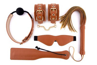Ett BDSM-set med namnet "BDSM Set Veganskt Läder Cognac" med en klocka, handledsmanschetter, piska, ögonbindel och paddel visas på en vit bakgrund.