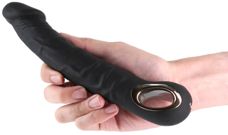 En hand håller i Rimmer Black Dildovibrator, en svart böjd vibrator tillverkad av kroppssäker silikon, med ett metalliskt ringhandtag.