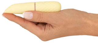 En hand håller den eleganta, beige Mini Vibrator Cuties Gul med ett texturerat grepp och flera vibrationslägen. Den lätt vinklade designen parar sig elegant med manikyrerade naglar i ljusrosa lack, vilket förstärker den lyxiga känslan av denna silikonmassager.
