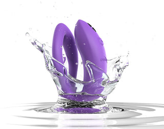 WE-Vibe Sync O Vibrator, en elegant, böjd enhet i lila, stänker i klart vatten med dynamiska droppar på en vit bakgrund. Dess design visar upp vattentäthet och modern teknik, sömlöst integrerad med We-Vibe-appen för förbättrad anslutning.