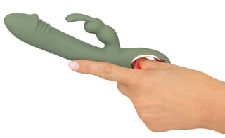 En hand håller Slim Rabbit Vibrator Olive i livfull grön silikon, designad med en böjd spets och dubbla stift för dubbel stimulering. Handtaget har en elegant metallic accent, allt mot en vanlig vit bakgrund.