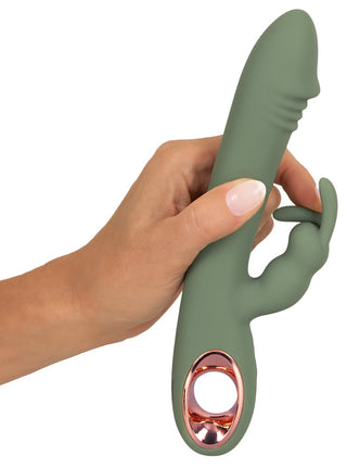 En hand håller Slim Rabbit Vibrator Olive, tillverkad av silkeslen silikon. Den har en elegant design med ett böjt huvudskaft med texturerade linjer och en mindre extern stimulator. Basen har en metallisk roséguldaccent med en öppen cirkulär design för dubbelstimulans.