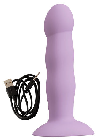 En lavendel Heart Guy Purple Dildo Vibrator med en rundad spets och bred bas står upprätt bredvid en svart USB-laddningskabel.