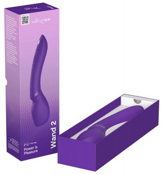 We-Vibe Wand 2 i lila, med sin böjda design och Smart Silence-teknik, utlovar en skonsam, brusfri upplevelse. Den visas bredvid sin förpackning och framhäver varumärkeslogotypen, produktbilden och sloganen "Power is Pleasure" medan den ligger perfekt inbäddad i den öppna lådan.