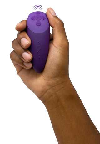 En hand håller i en We-Vibe Chorus Parvibrator fjärrkontroll med knappar, med en ikon för trådlös signal ovanför.