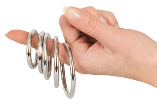 En hand med fransk manikyr balanserar elegant fem Metall Penisringar på pekfingret.