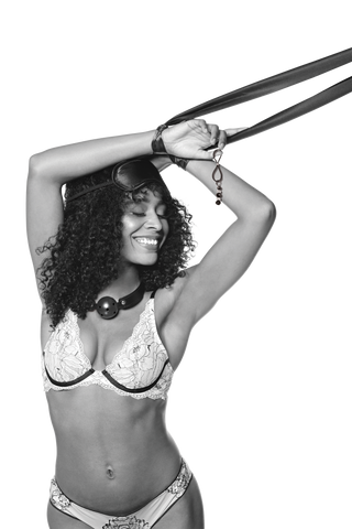 Leende kvinna i underkläder med aviatorglasögon lyfter armarna - perfekt inspiration för en nybörjare som utforskar den lekfulla sidan av BDSM med Bondage Kit Svart 5-delar.