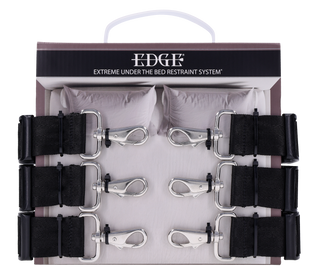 Edge Restraint System Säng erbjuder justerbara svarta bondage-remmar och manschetter, boxade för den som söker dominans. Två kuddar i bakgrunden antyder diskret förvaring eller lekfull förväntan.
