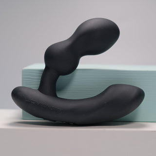 Den eleganta svarta Lovense Edge 2 - Prostata Vibrator, med sin ergonomiska böjda design, visas elegant på ett ljusblått block ovanpå en orörd vit yta.