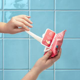 En person drar ut en EasyGlide Intimservetter 25-pack våtservett från en rosa förpackning mot en ljusblå kaklad vägg.