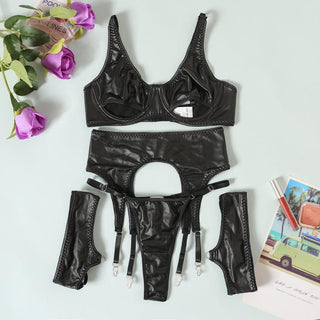 WetLook Lingerie Bh-Set visar upp en svart läderbh, strumpeband, stringtrosa och manschetter på en ljus yta, omgiven av lila rosor och resevykort som framkallar en sensuell upplevelse som transporterar dig till avlägsna platser.
