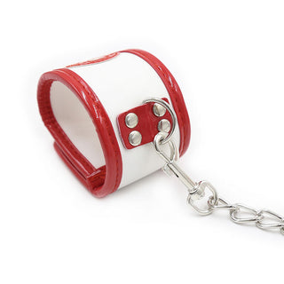 Ohmama 3-delade Nurse Bondage Set innehåller en handledsmanschett i vitt och rött läder med metalldubbar, med röd trimning och en D-ring med en kedjeklämma, perfekt för äventyrliga rollspel.