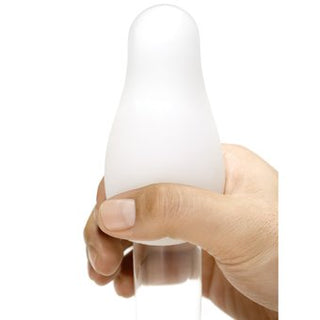 En hand håller försiktigt en Tenga Thunder onanist, med en vit, rundad design med en transparent bas, mot en orörd vit bakgrund.