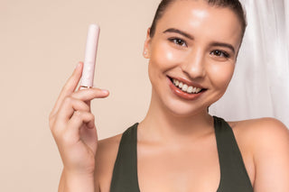 Leende kvinna i grönt linne håller upp en ljusrosa vibrator i en ljus och avslappnad miljö, idealisk för kategorin vibratorer