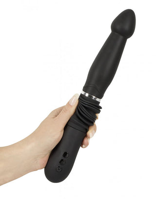 En hand håller You2Toys Thrust Vibrator, en svart silikondildo med knappar och en räfflad basdel, som erbjuder kraftfulla vibrationer för en intensiv upplevelse.