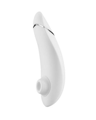 En elegant vit handhållen Womanizer Premium 2 har Pleasure Air™-teknik, en böjd design med en liten cirkulär öppning i botten och ett tunt metallband som accentuerar toppen. Dess moderna utseende ställs mot en vanlig vit bakgrund.