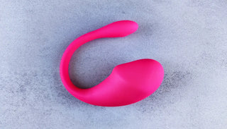 Rosa klitorisvibrator i silikon med böjd form, fotograferad mot ljus bakgrund