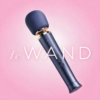 Le Wand massagewand i mörkblått med roséguldfärgade detaljer, mot en mjuk rosa bakgrund med vit Le Wand-logotyp.