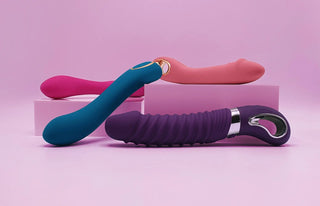 Fyra stilrena G-punktvibratorer i olika färger och former placerade på rosa bakgrund med dekorativa block, optimerad för mobilvisning av G-punktvibrator-kategorin