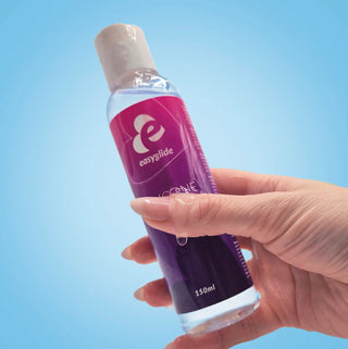 Hand som håller i en flaska Easyglide silikonbaserat glidmedel, 150 ml, mot blå bakgrund