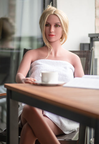 Realistisk sexdocka, 168 cm, tillverkad i TPE med naturtrogen design. Produkten visas sittande vid ett bord.