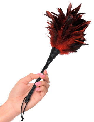 En hand håller i Frisky Feather Tickler, en liten svart och röd fjäderdoftare med svart handtag och handledsrem.