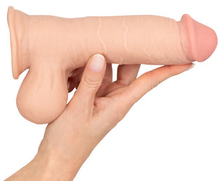 En hand som håller en Nature Skin Realistisk Dildo 20 cm mot en vanlig bakgrund.