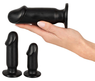 En hand håller en stor plugg från Analsex Training Set med två mindre svarta silikonpluggar i närheten.