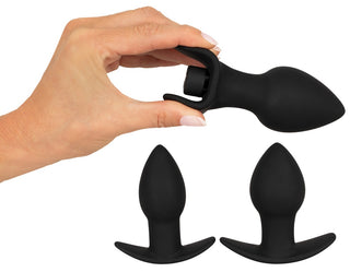 En hand håller en Black Velvets 3-Delat Buttplugset-plugg, tillverkad av silikon med en mjuk textur; två ytterligare pluggar från setet visas nedan.