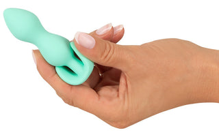 En hand håller Cuties Mini Buttplug Grön, gjord av kroppssäker silikon, med en utsvängd bas och en elegant, böjd design i livfull teal.