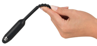 En hand håller Dilator Vibe Vibrerande Stimulator, en svart silikonleksak med pärlor, mot en vit bakgrund.