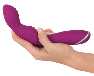 En hand håller Sweet Smile - A & G-Punkts Vibrator, en lila böjd silikonenhet för G-punkt-stimulering, med 7 vibrationslägen mot en vanlig bakgrund för en utforskning av nöje.