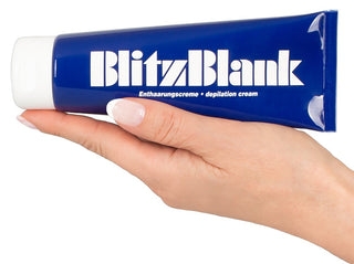 En hand håller en blå tub av BlitzBlank Hårborttagningskräm, berikad med närande ingredienser, med en vit mössa och skarp vit text som lovar silkeslen hud.