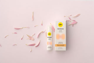 En flaska och ask Woman Lust Intense gel, en klitorisstimuleringsgel för intensiv njutning, omgiven av spridda rosa kronblad på en ljus bakgrund.