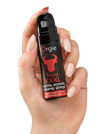 En hand håller en svart flaska märkt "Touro XXXL Power Cream" för män, med en red bull-grafik och formulerad med ginseng som stimulerande massagekräm för effektiv penismassage.