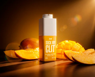 En flaska Intt Suck My Clit Tropical Mango, med en gul etikett och genomskinlig plast, uppställd på högkant.