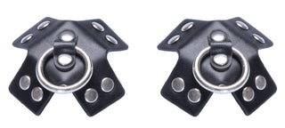 Nipple Stickers X-form Läderlook - två svarta BDSM-accessoarer i konstläder med metallringar och nitar, arrangerade sida vid sida som slående bröstvårtsklistermärken mot en vit bakgrund.