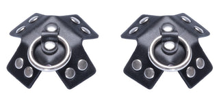 Nipple Stickers X-form Läderlook - två svarta BDSM-accessoarer i konstläder med metallringar och nitar, arrangerade sida vid sida som slående bröstvårtsklistermärken mot en vit bakgrund.