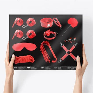 Händer som håller en tavla som visar IntoYou 10-Delar Bondage Kit, med röda BDSM-tillbehör som manschetter, ögonbindel, ball gag och rep mot en svart bakgrund.