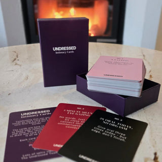 En låda med kortleken Undressed Intimacy Cards Kortlek ligger på ett bord, med flera kort för par utspridda - perfekt för att stärka ditt band och inspirera till djupare kontakt.