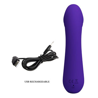 En lila elektronisk enhet, Mjuk Lila Vibrator Cetus med rundade kanter, sitter bredvid en svart USB-laddningskabel. Symboler och text på sidan indikerar att den är USB-uppladdningsbar.