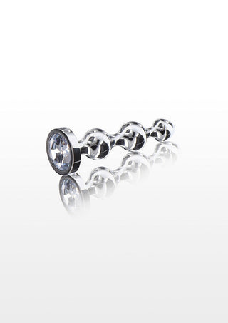 ToyJoy Diamond Star Beads har en silverkedjeliknande design med sammankopplade öglor och en transparent cirkulär ädelsten i ena änden, som reflekteras elegant på en vit yta. Tillverkad av nickelfritt aluminium, dess moderna estetik påminner om en dekorativ juvel.