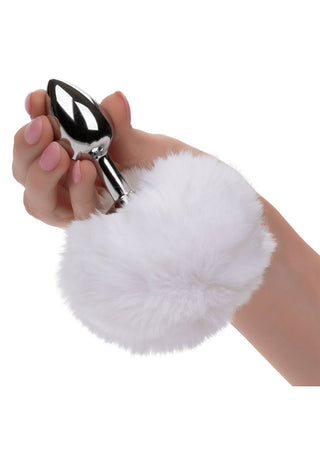 En hand med ljusrosa nagellack håller ömtåligt Fluffig Analplugg med Svans, med en mjuk, fluffig pom-pom som påminner om en kaninsvans, mot en krispig vit bakgrund.