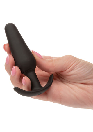 En hand med rosa naglar håller i Boundless Vibrating Slim Plug, en analplugg i svart silikon, mot en vit bakgrund.